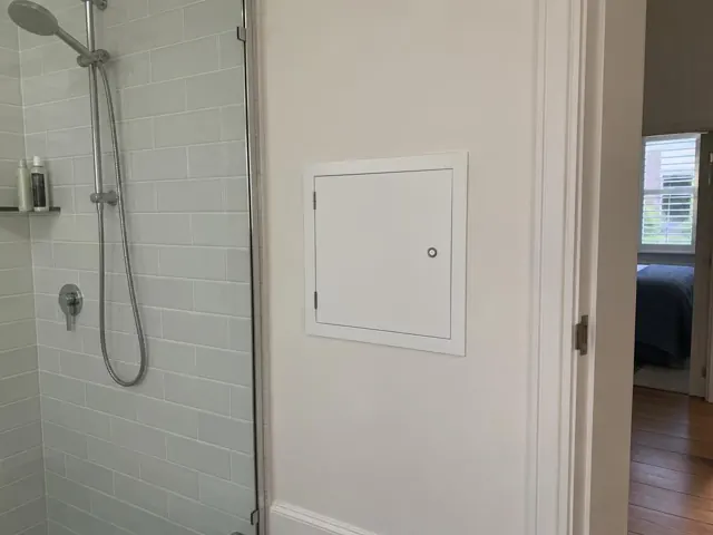 Small access panel on a painted bathroom wall beside a tiled shower in Double Bay
